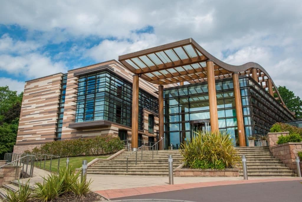 Modern corporate event venue featuring a glass facade, wooden canopy entrance, and landscaped steps.