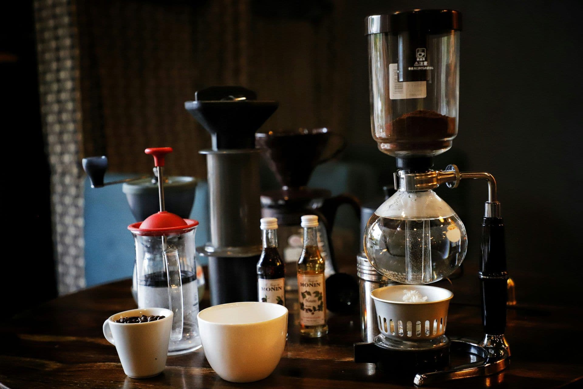 Siphon coffee brewer, French press, and cups on a table, ready for a corporate coffee workshop or team