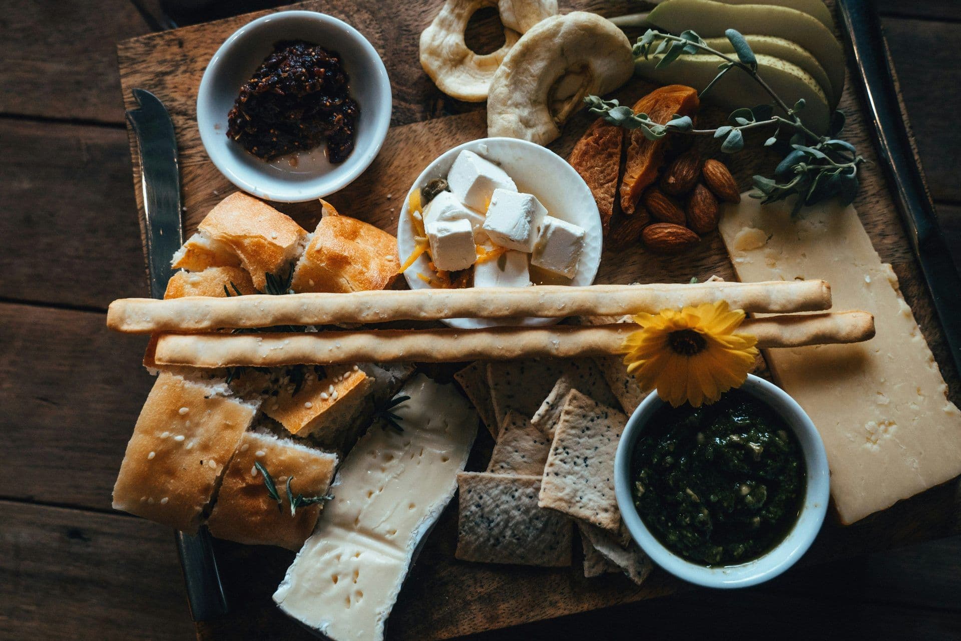 Overhead view of a gourmet cheese and bread board with dips, nuts, and fruit