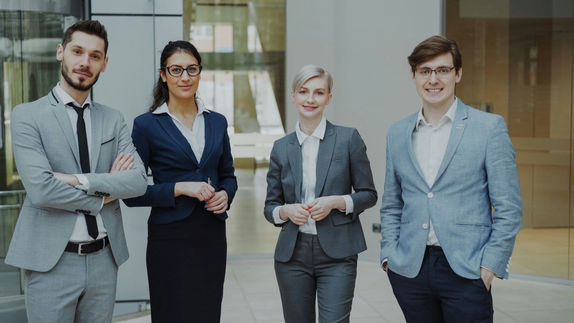 Four smiling business professionals, two men and two women, standing in a modern corporate event venue.