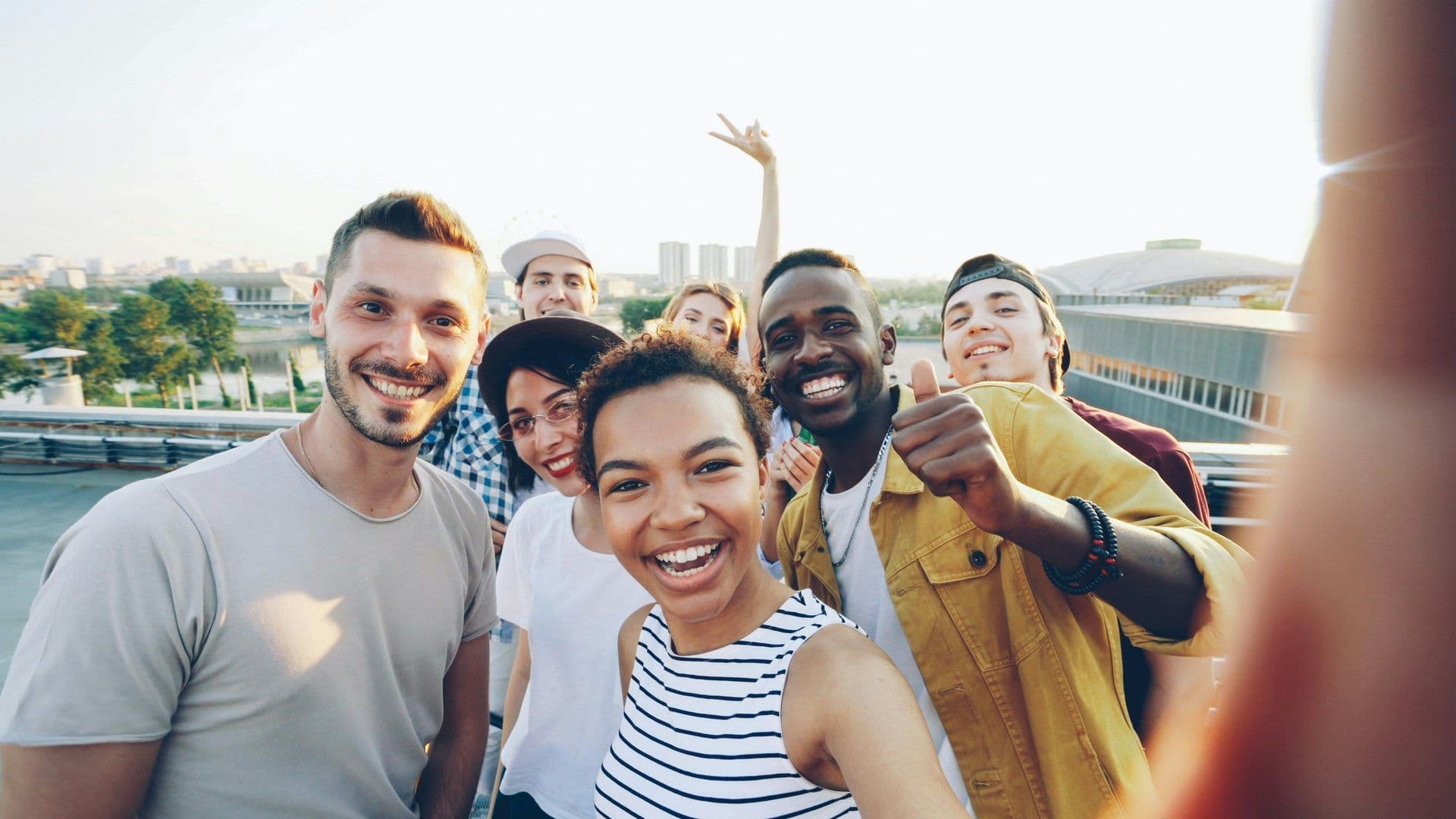 Smiling diverse team enjoying a company away day selfie on a rooftop event space with city views.