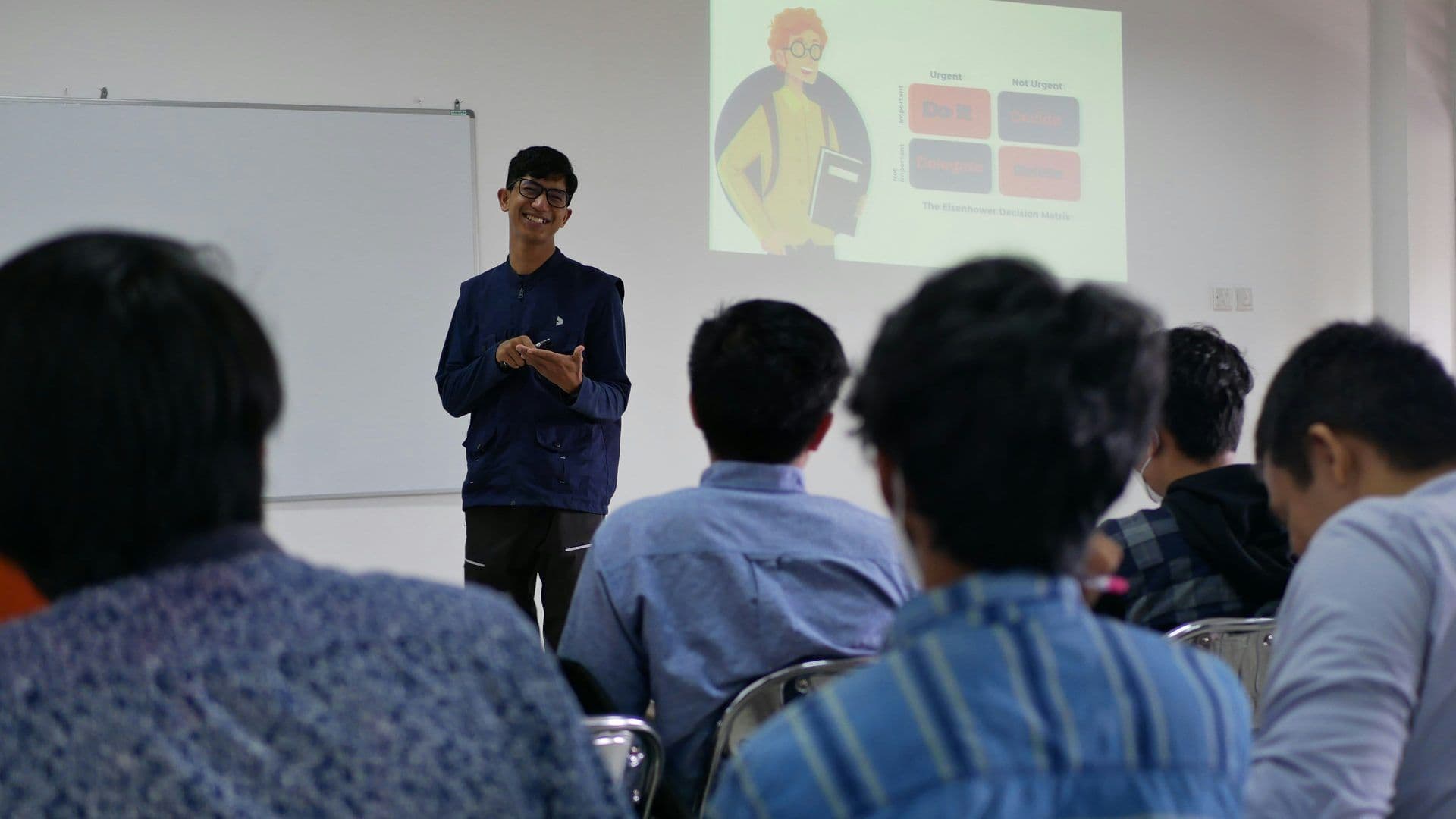 A young man presents the Eisenhower Decision Matrix on a projector screen during a corporate workshop.