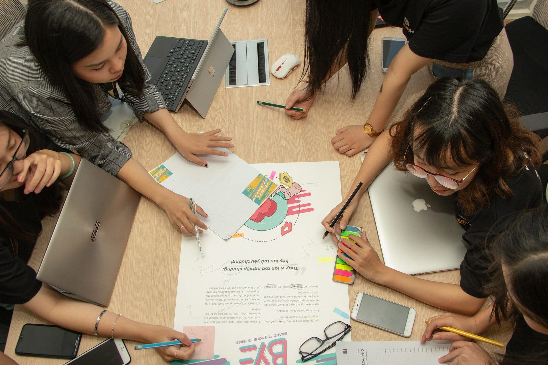 Overhead view of colleagues collaborating on laptops and documents at a modern meeting room table.