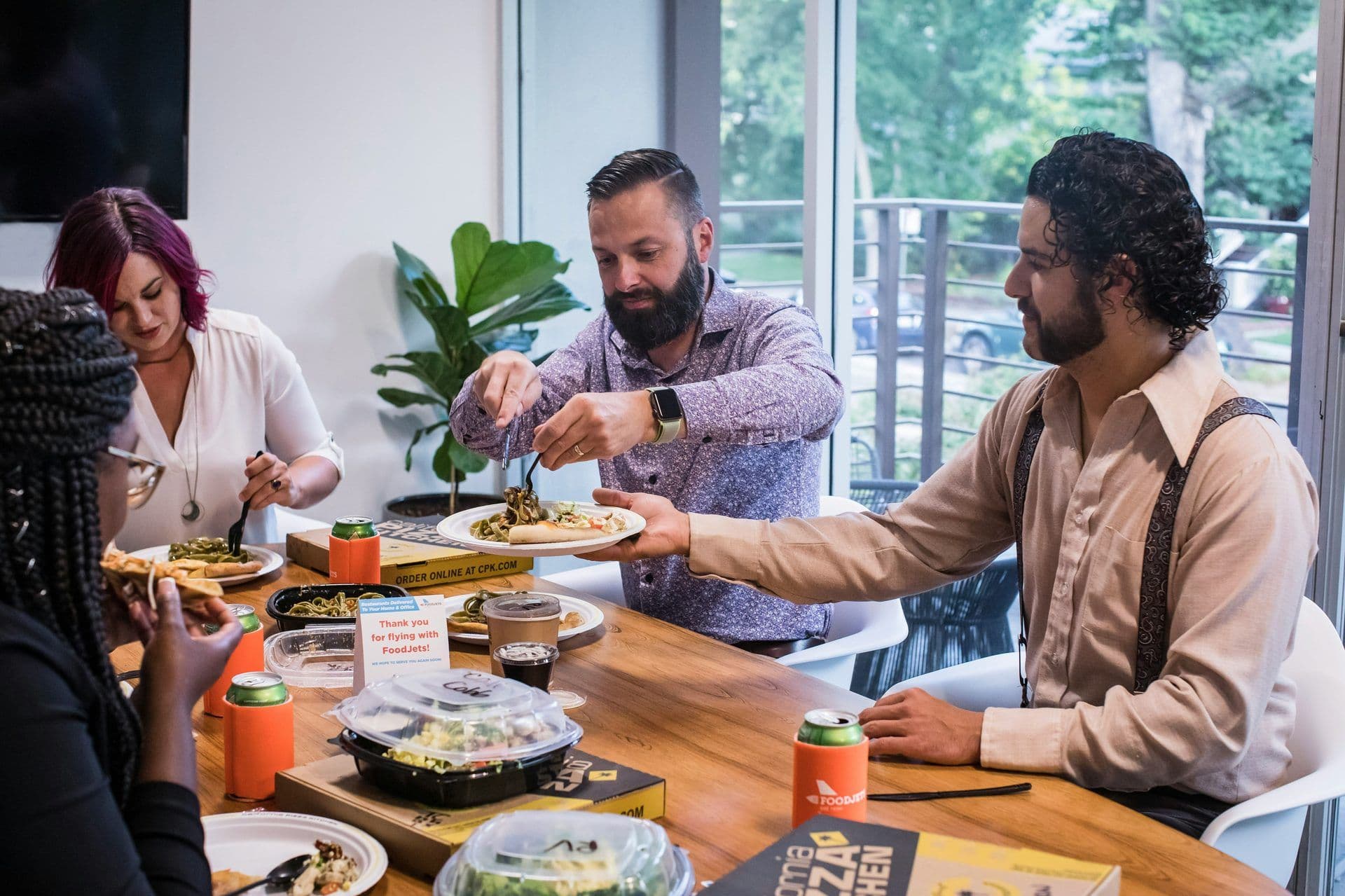 Four colleagues enjoy a catered business lunch in a modern meeting room with a large window.