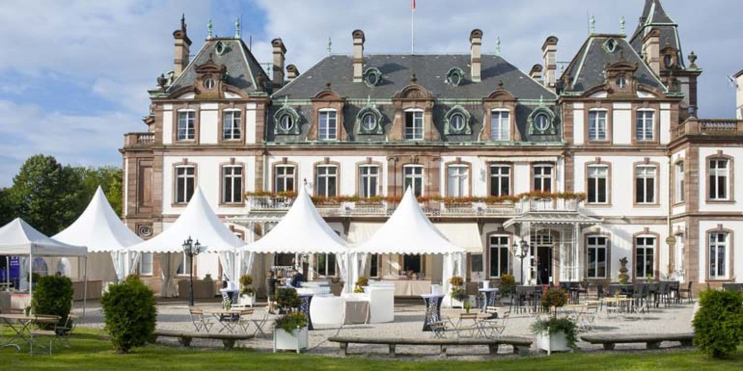 Historic chateau with white event tents and outdoor seating on a green lawn, perfect for corporate events.