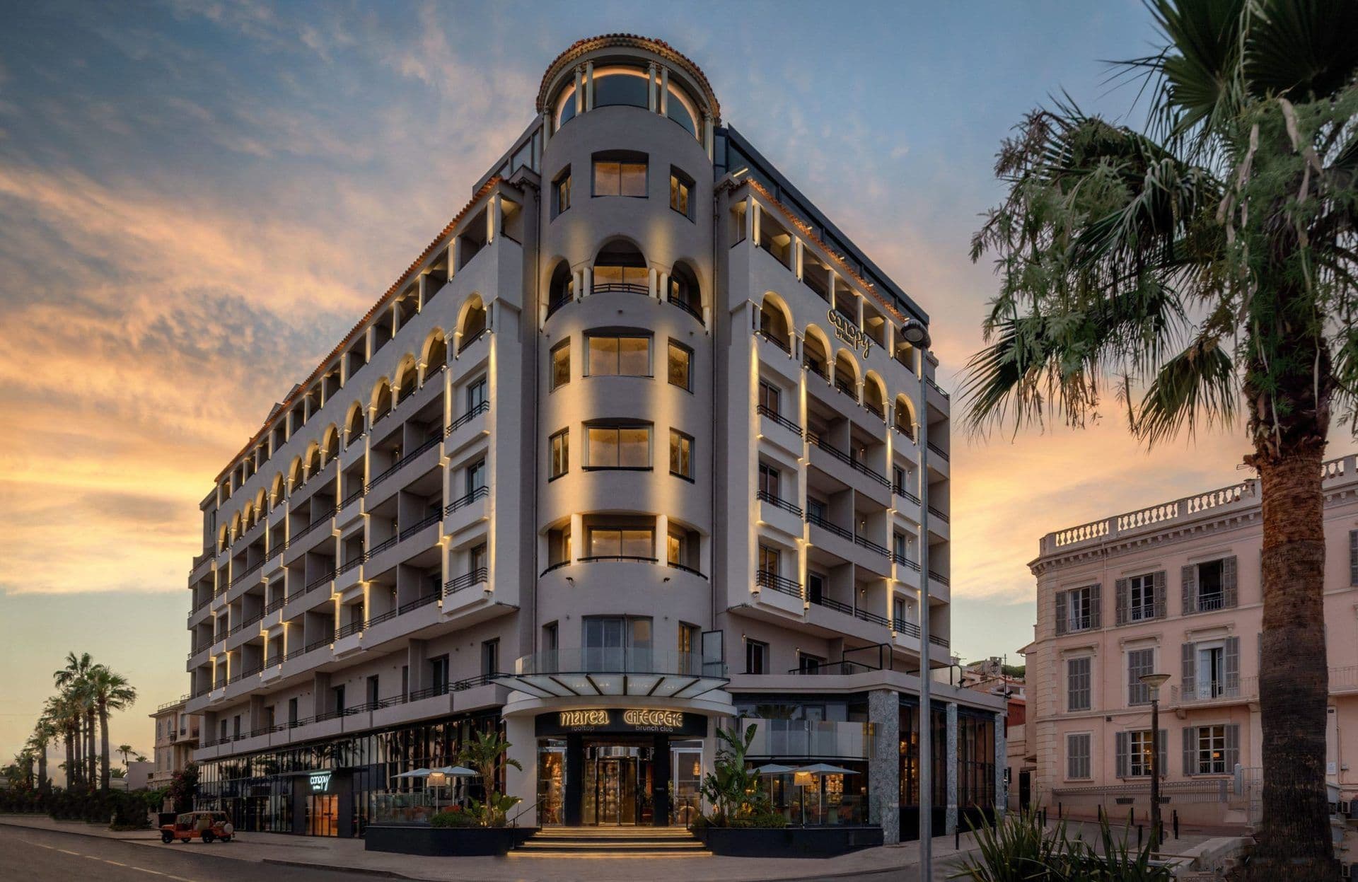 Modern hotel and corporate event venue with warm lighting, arched balconies, and palm trees at dusk.