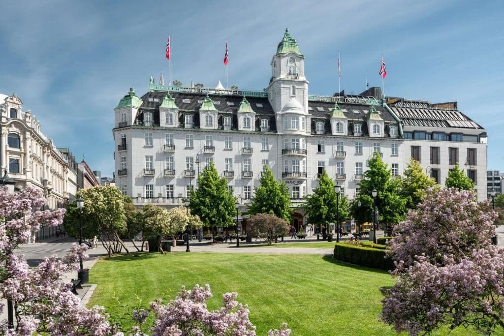 Grand Hotel Oslo, a historic corporate event venue, overlooks a vibrant park with flowering trees.