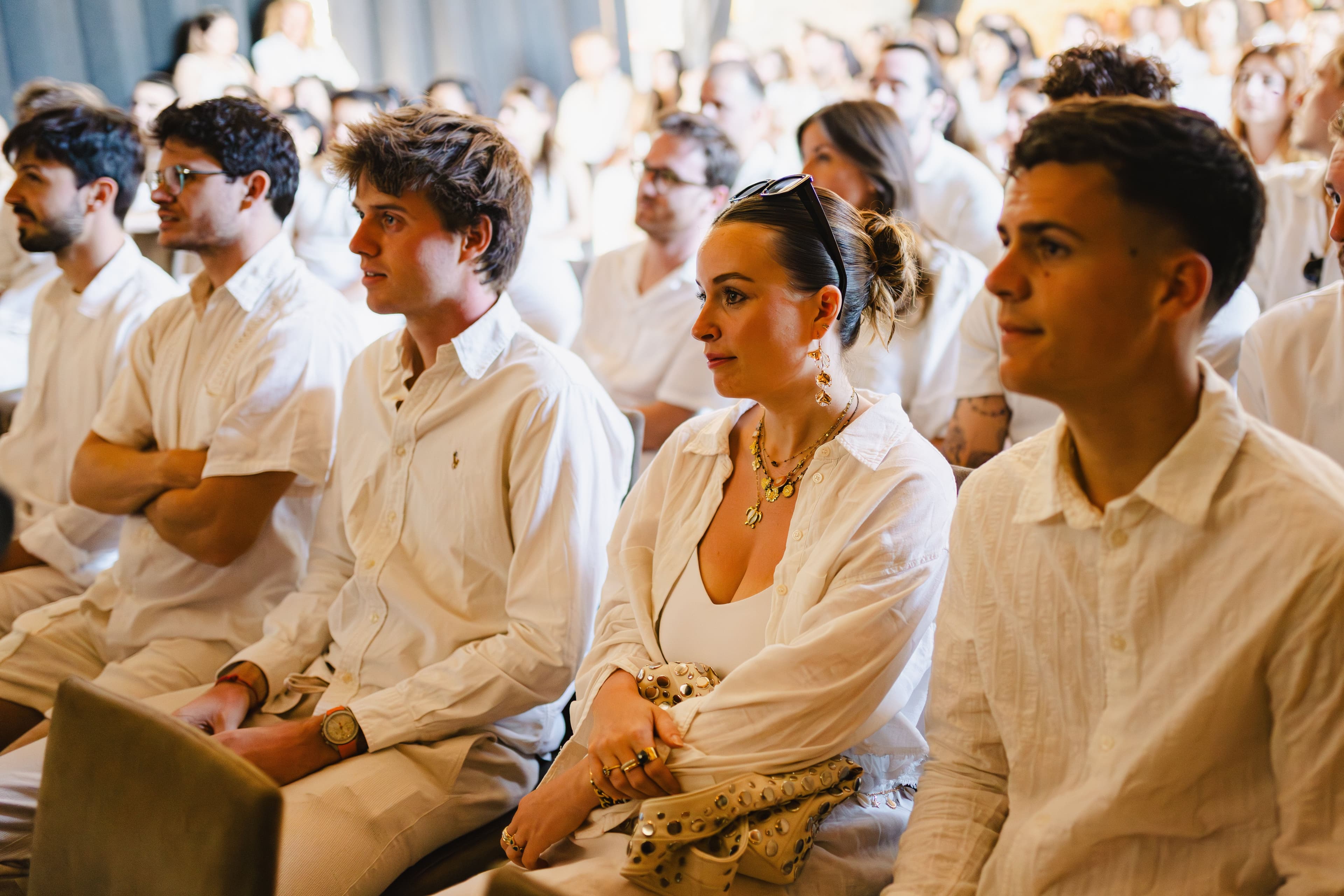 Attendees in light clothing sit engaged during a corporate seminar or large group event.