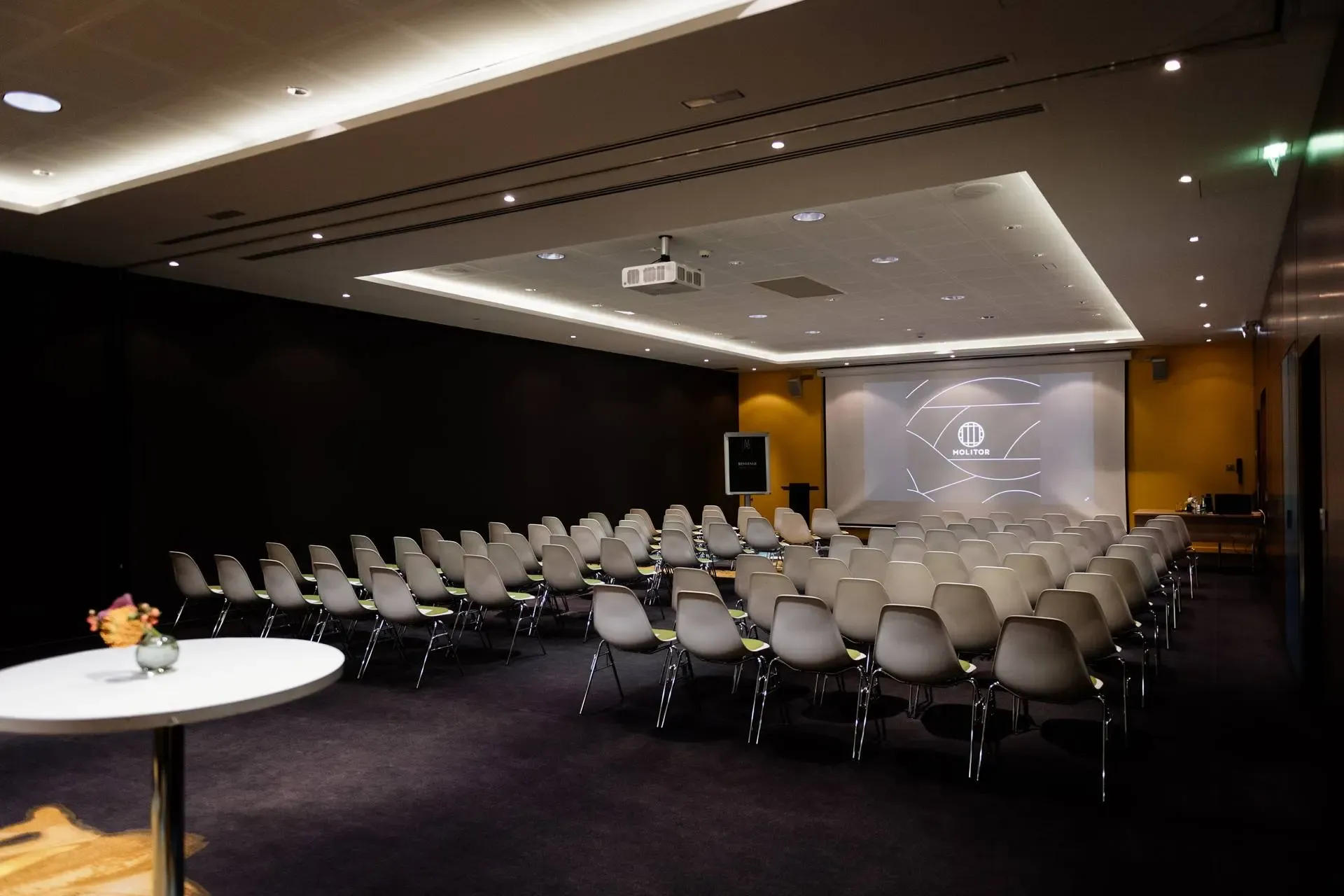 A modern corporate seminar room with rows of chairs facing a large projection screen and projector.