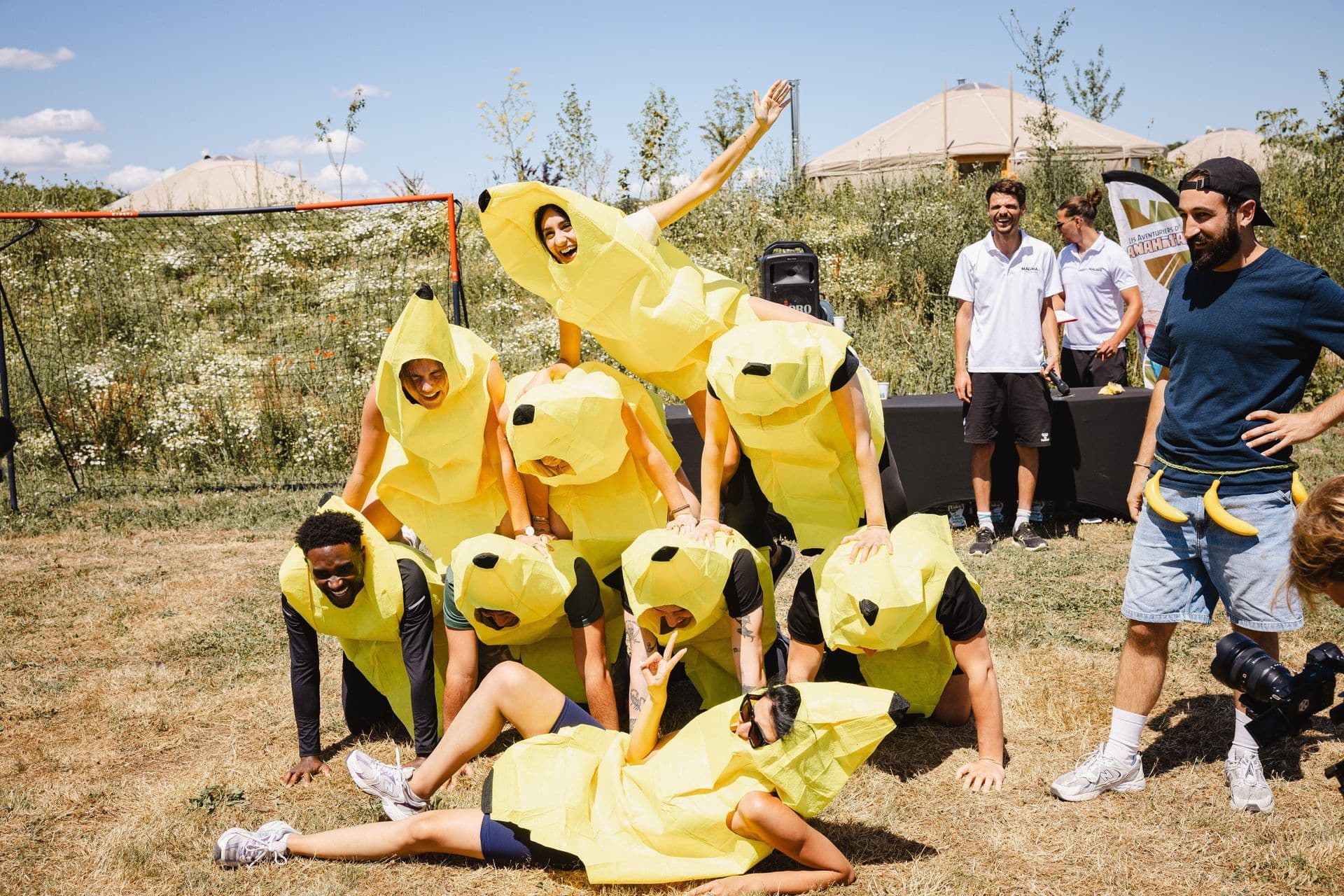 Employees in banana costumes form a human pyramid during an outdoor team building activity.