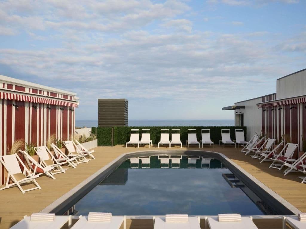 Rooftop swimming pool with lounge chairs, wooden deck, and ocean view, ideal for corporate retreats.