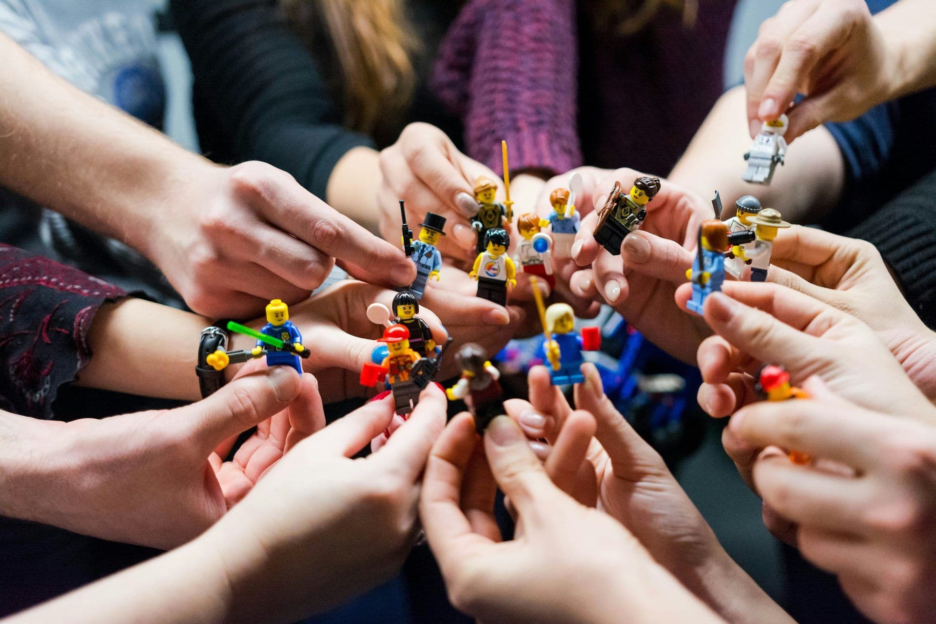 Many hands hold diverse Lego minifigures during a corporate team building workshop.