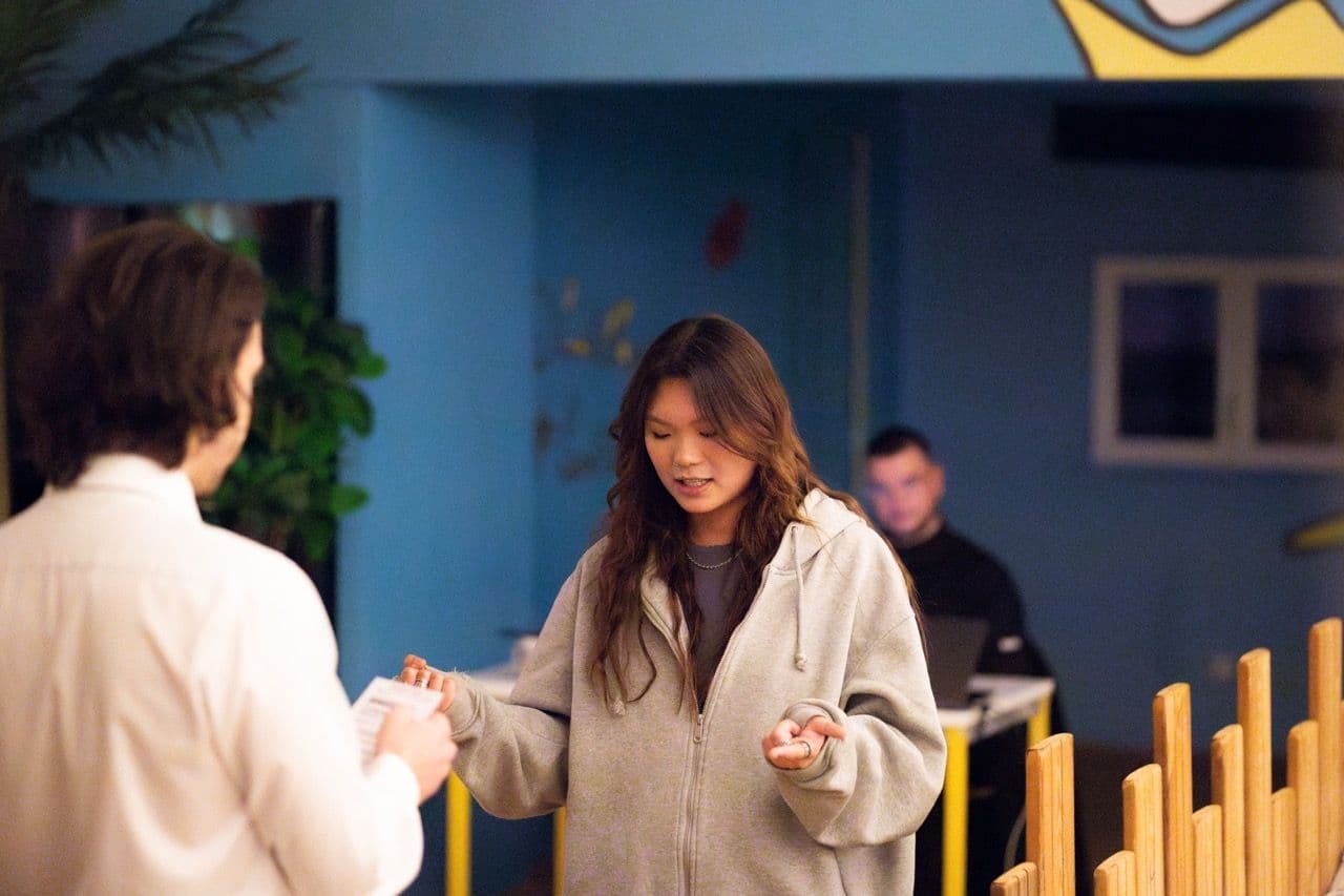 Two people exchanging items at a casual corporate event in a modern blue-walled venue.