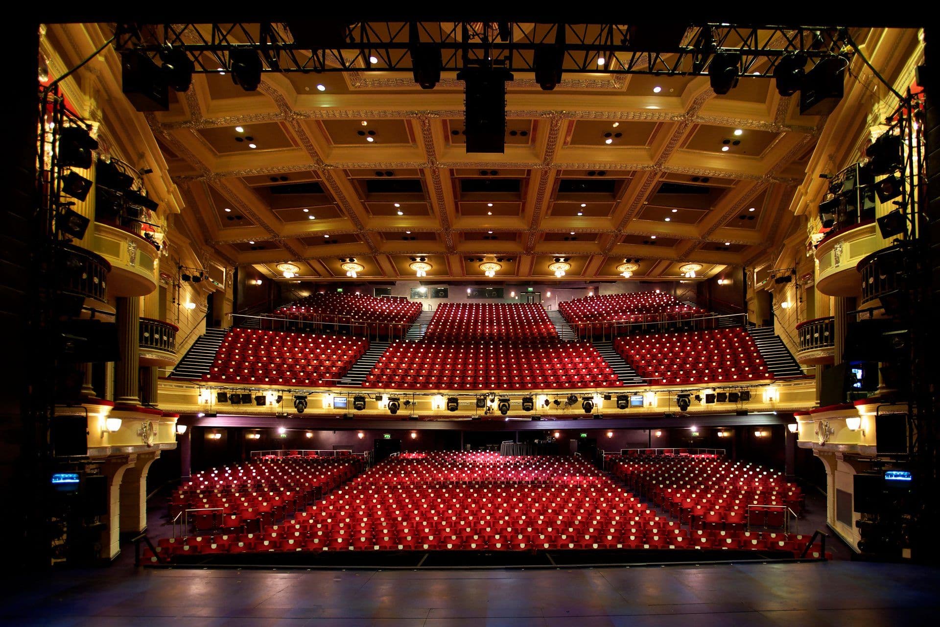 A grand auditorium with tiered red seating, an ornate ceiling, and a stage