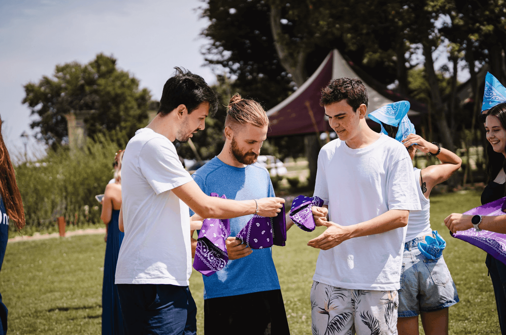 Young professionals distribute purple and blue bandanas during an outdoor team building activity.