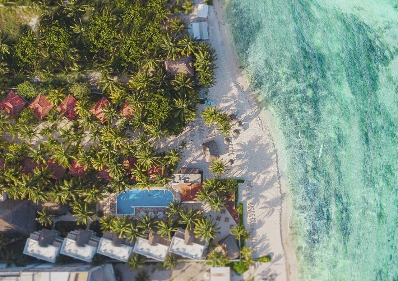 Aerial view of a tropical corporate retreat venue with palm trees, bungalows, a pool, and a turquoise beach.