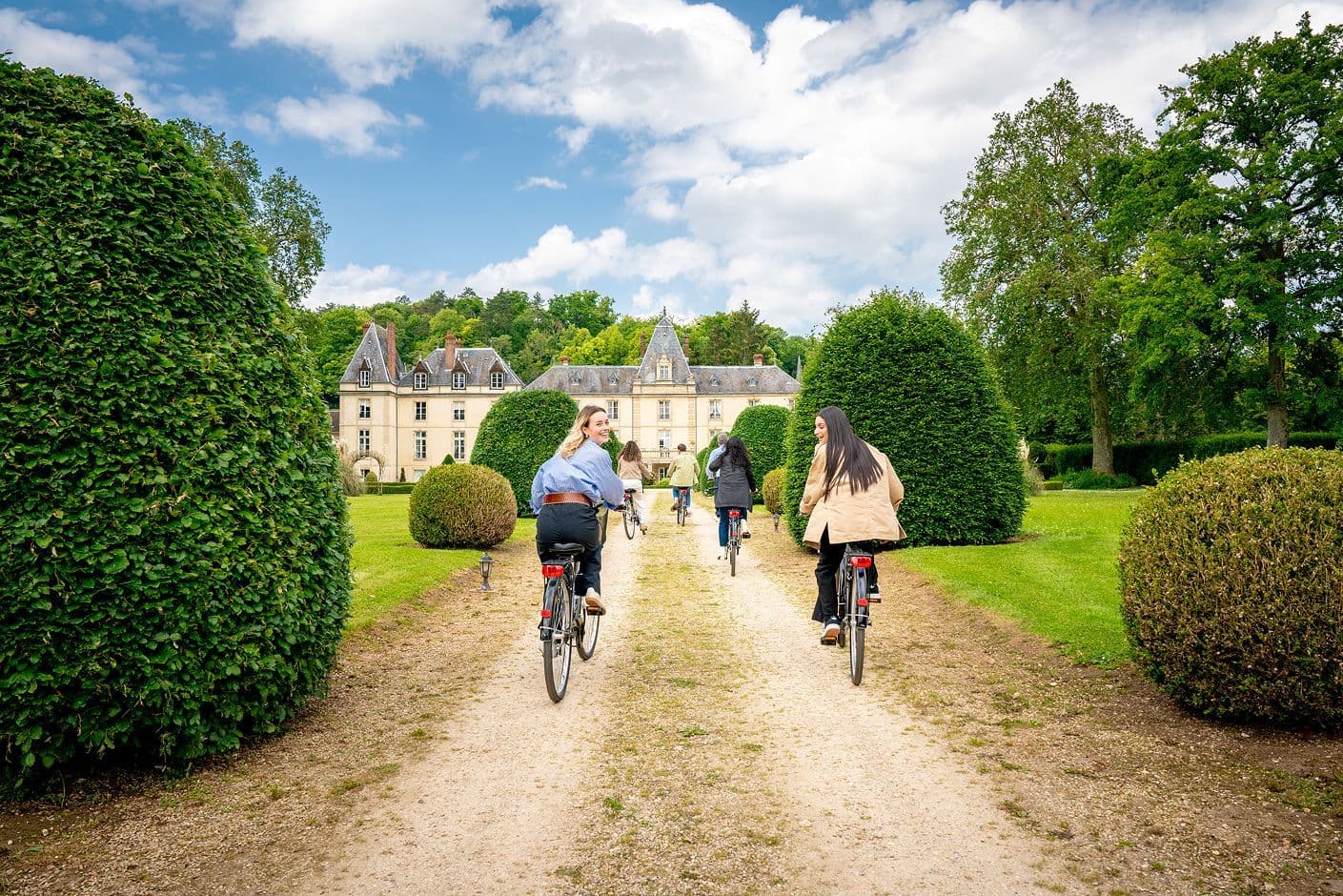 A group cycles on a gravel path towards a historic French chateau, perfect for a corporate retreat.