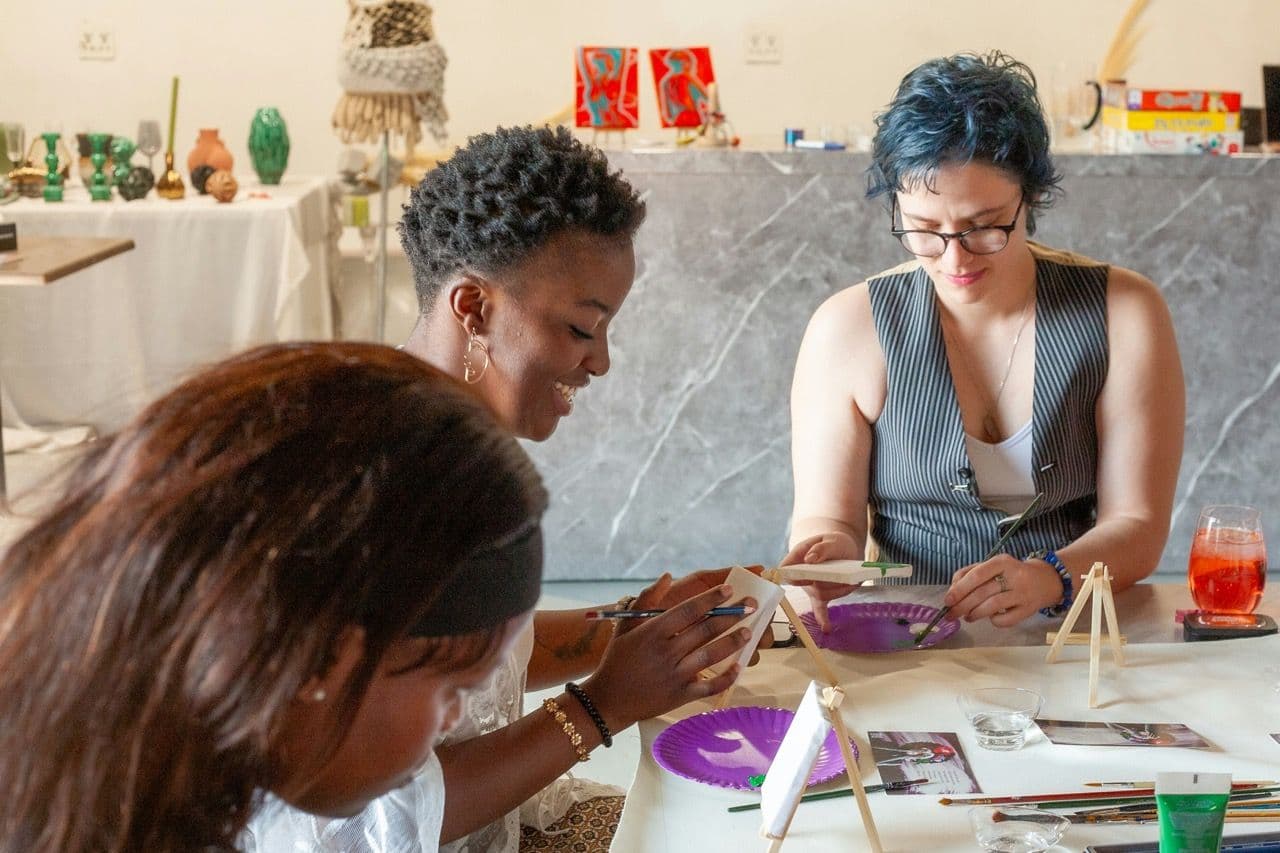 Three women participate in a painting workshop, a creative team building activity at a modern event space.