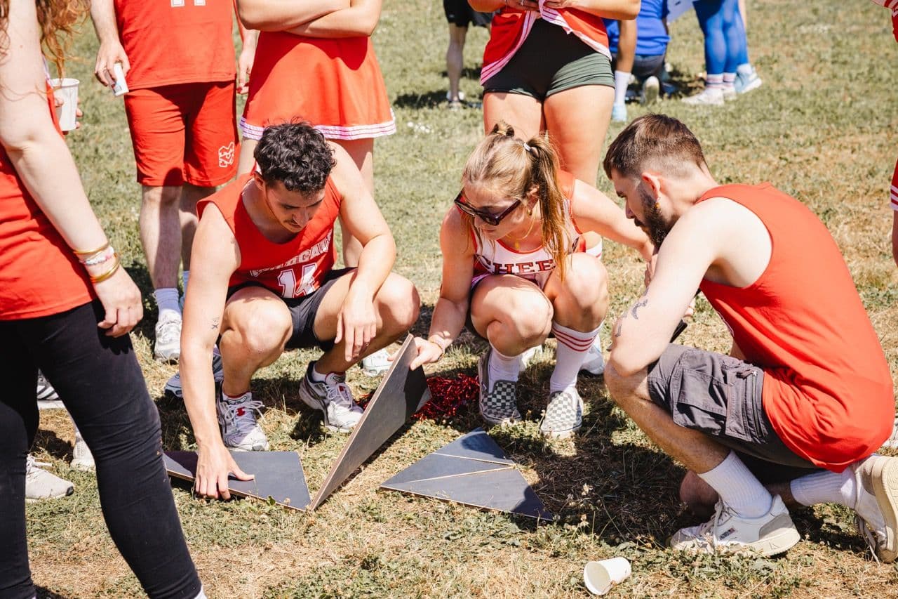 Three colleagues in red shirts collaborate on a wooden puzzle during an outdoor team building activity.