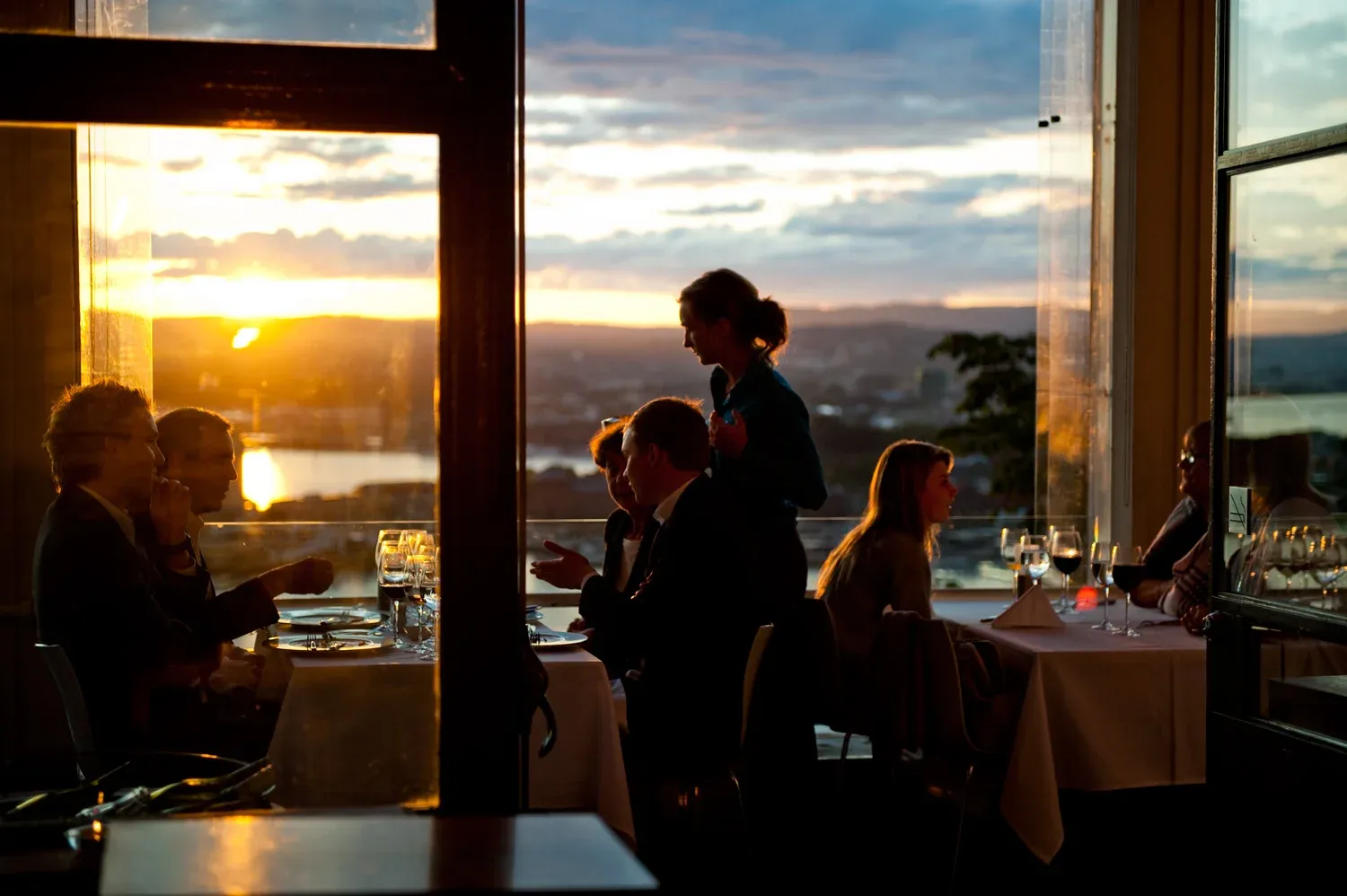 Business professionals enjoy a seated corporate dinner at a waterfront venue during sunset.