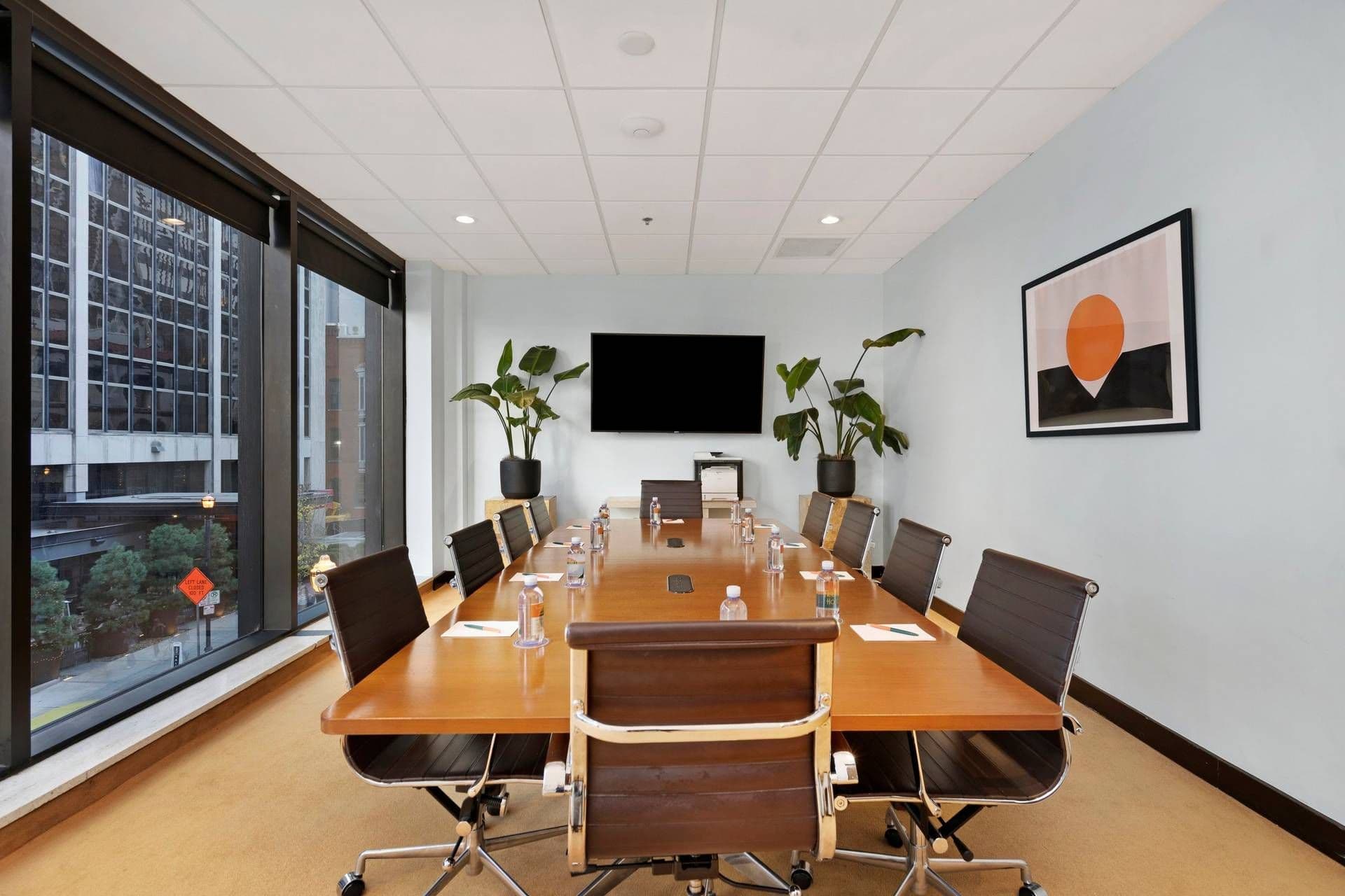 Modern boardroom with a large conference table, 12 chairs, TV, and city view, ideal for corporate meetings.