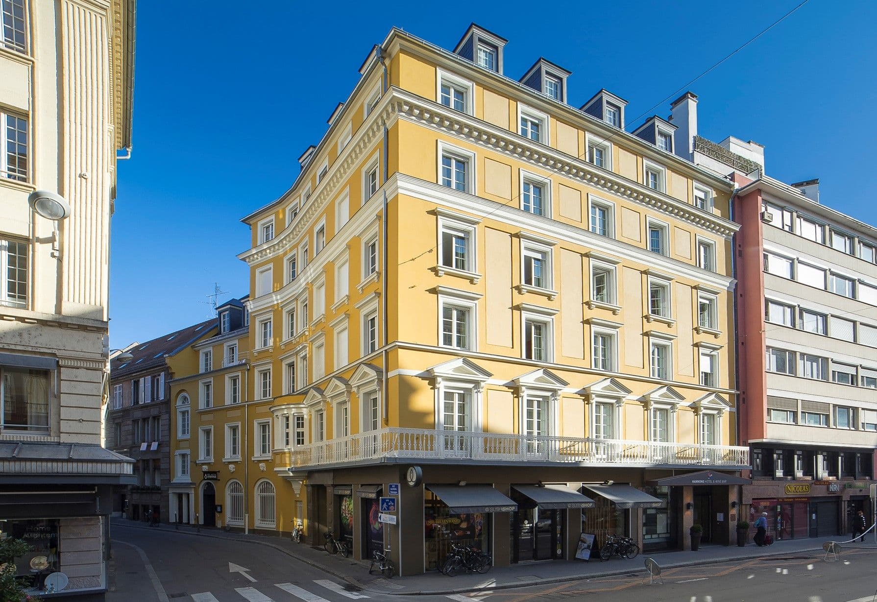 A bright yellow historic corporate event venue with a curved facade and balcony on a sunny city street.