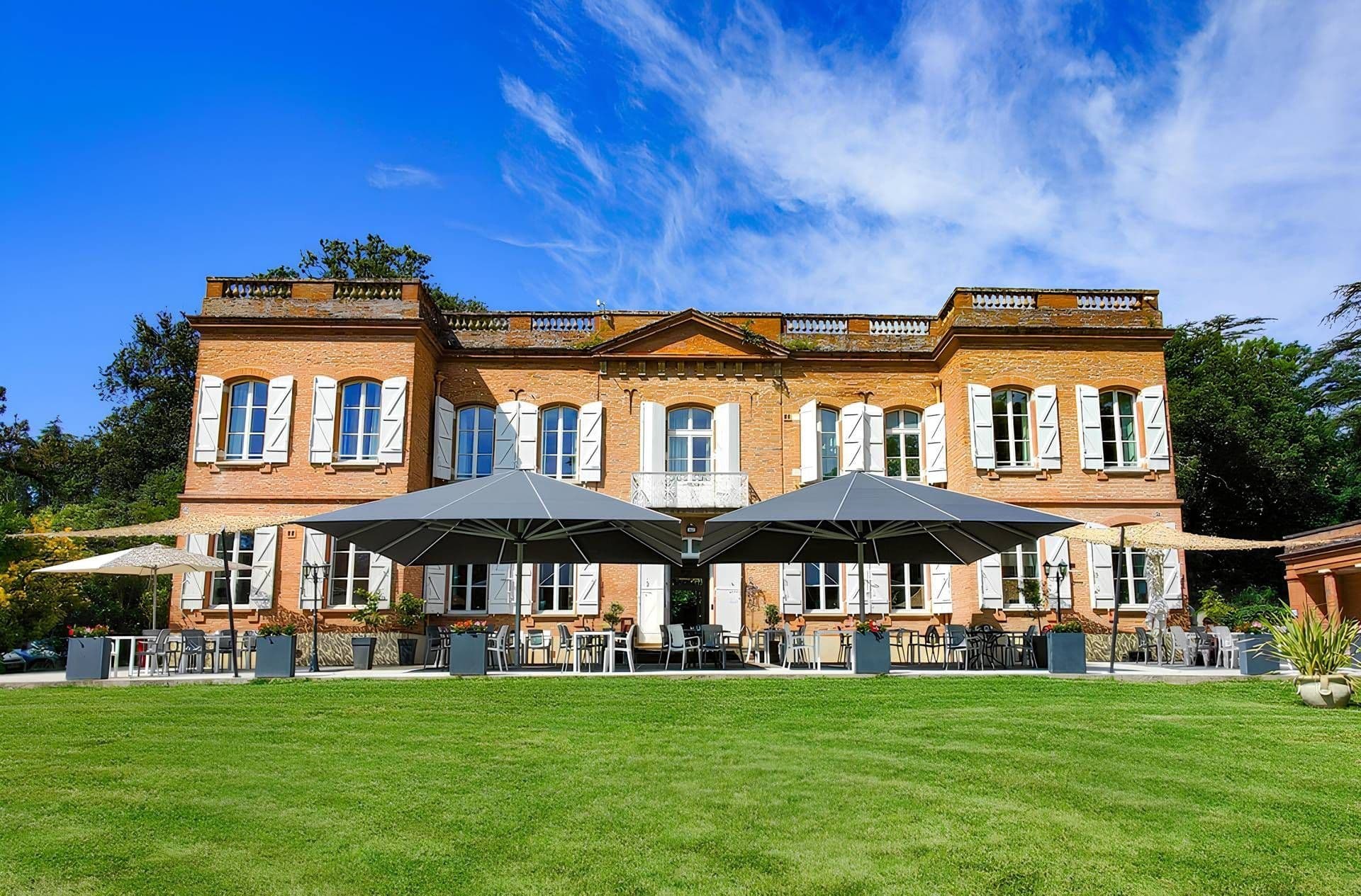 Historic corporate event venue with a spacious outdoor terrace, green lawn, and shaded seating.
