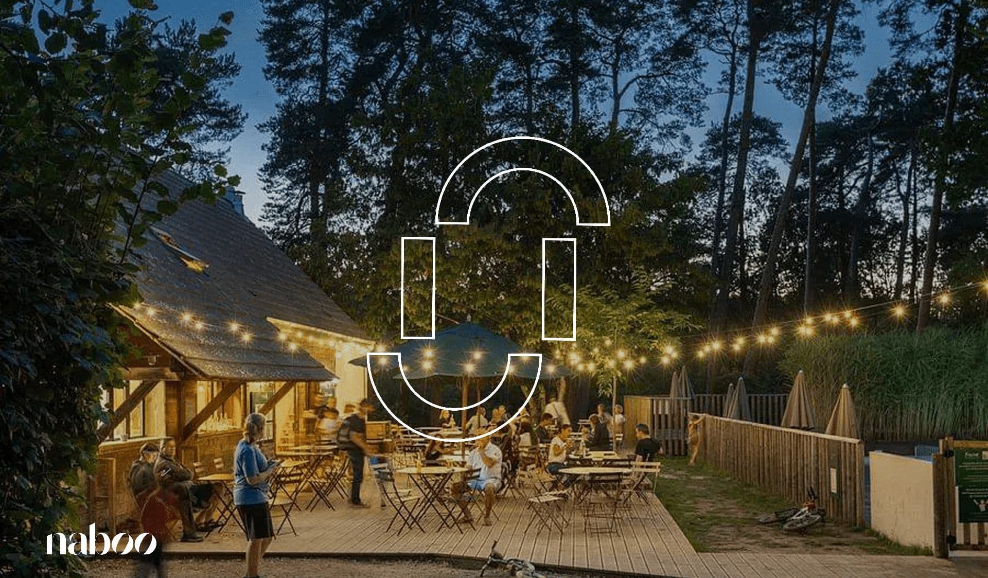 An illuminated outdoor event space at dusk, with guests on a wooden deck and a rustic lodge.