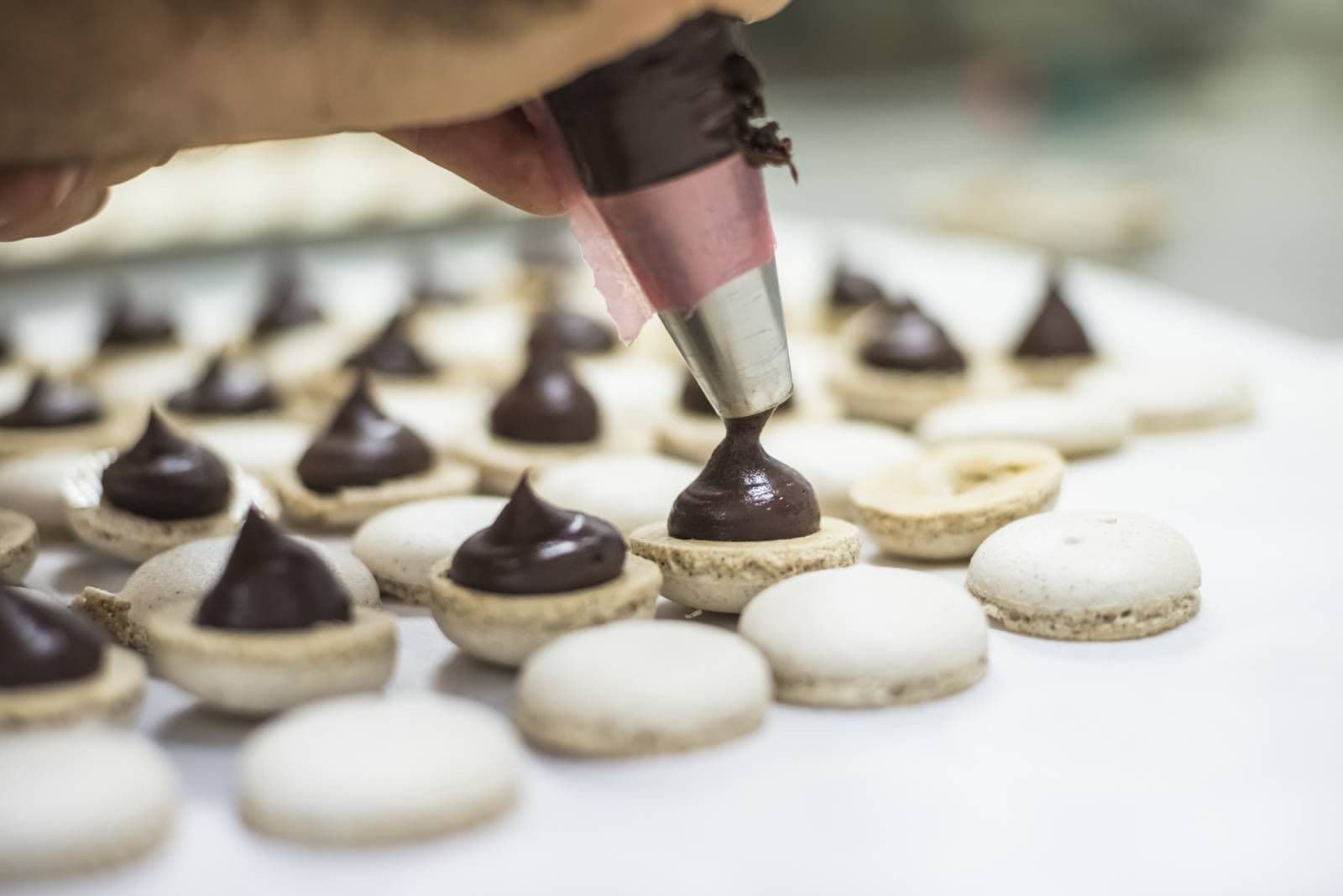 A hand pipes rich chocolate ganache onto delicate macaron shells during a cooking class team building