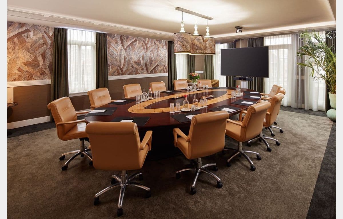 Elegant corporate meeting room featuring a large oval table, tan chairs, and a display screen.