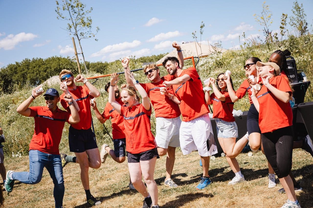 Energetic team in red shirts cheering during an outdoor corporate team building activity.