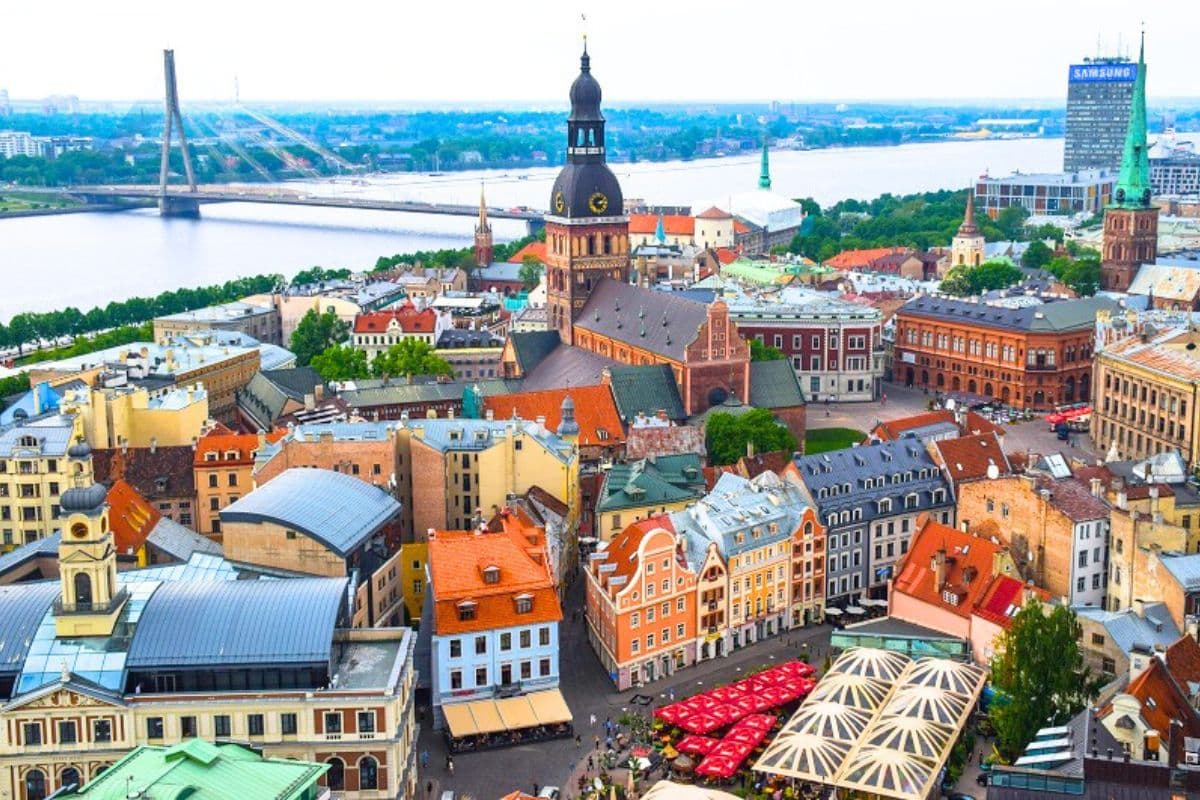 Aerial view of Riga, Latvia, featuring historic buildings, a church, and the Daugava River with a bridge.