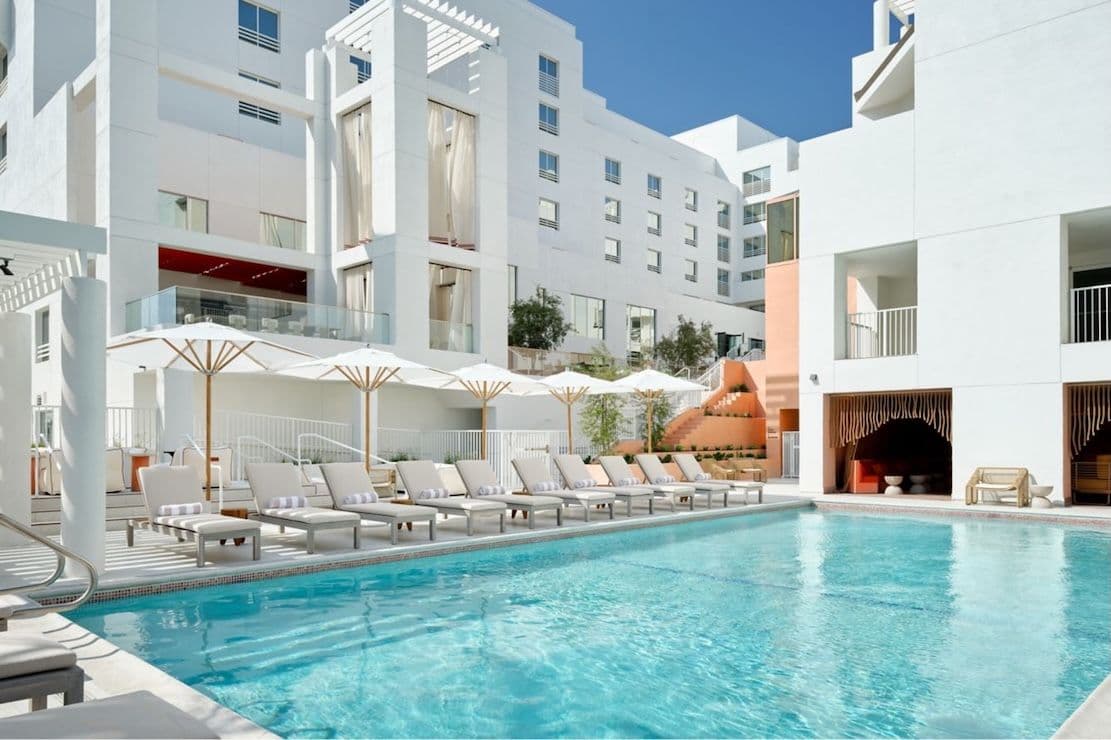 A modern white hotel pool area with sun loungers and umbrellas