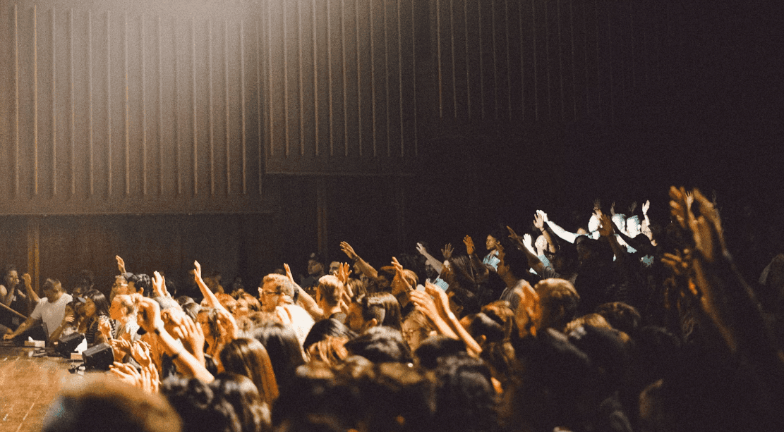 Attendees raise hands in a dark auditorium during a large enterprise event or corporate seminar.