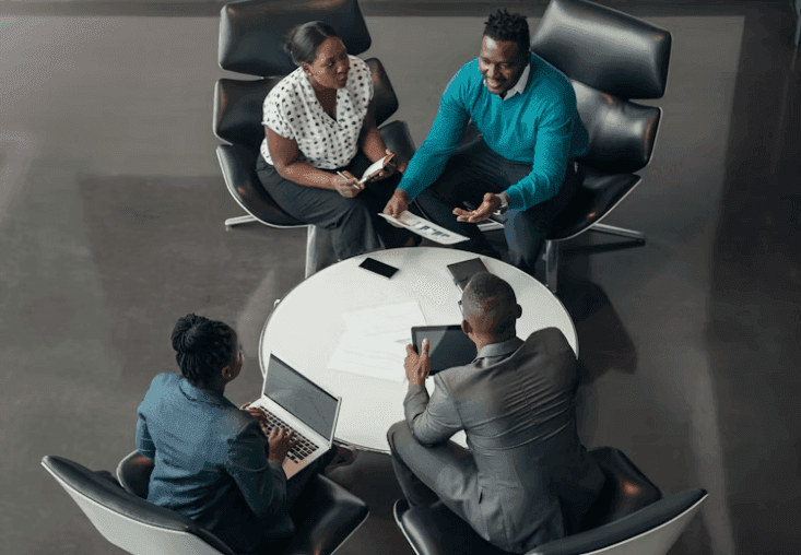 Four professionals discuss strategy around a table in a modern corporate meeting room.