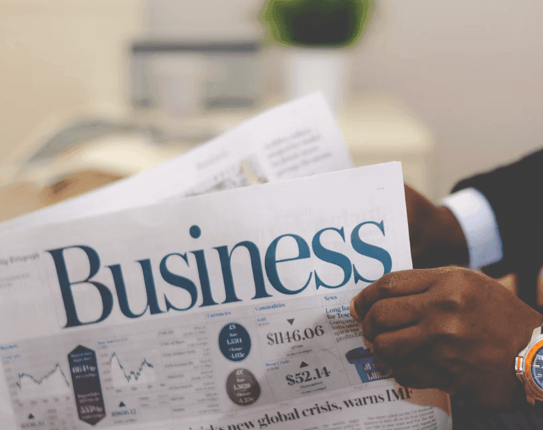 A professional reads the 'Business' section of a newspaper, displaying financial market data.