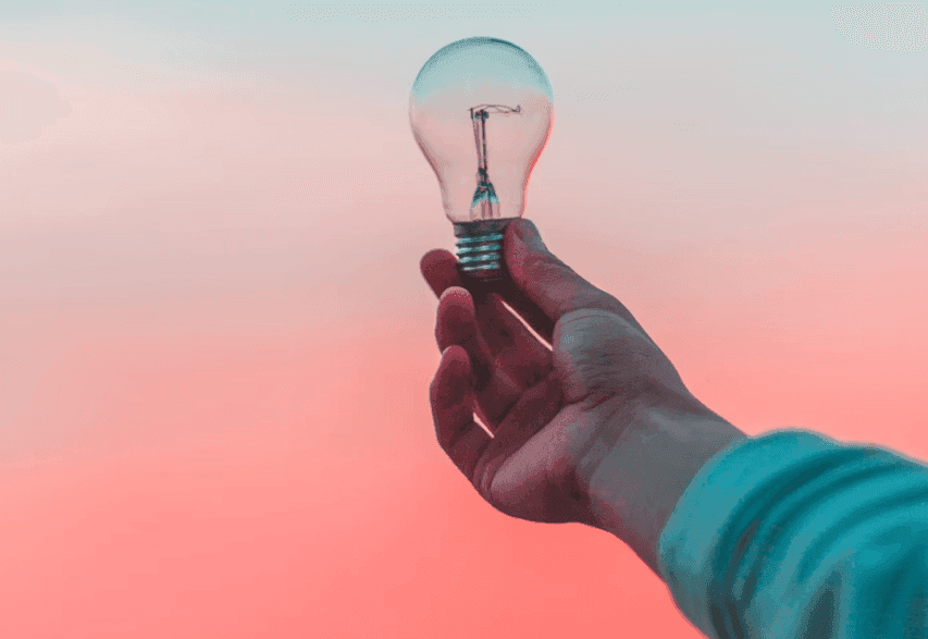 A hand holds an unlit lightbulb against a gradient sky, symbolizing innovative ideas for corporate workshops.