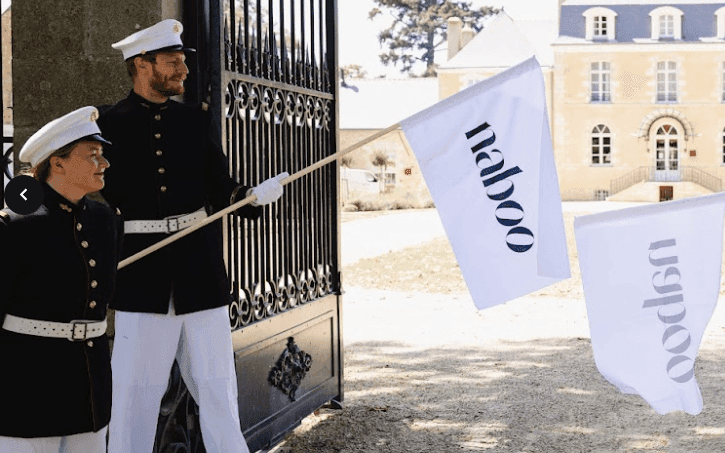 Uniformed staff holding Naboo flags welcome guests at the ornate gate of a grand historic corporate event