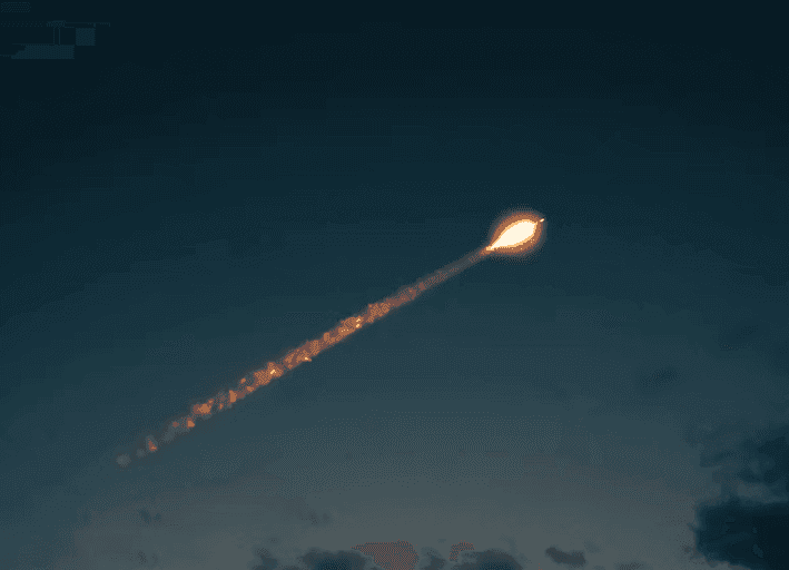 A bright, glowing light source with an elongated trail against a dark evening sky and subtle clouds.