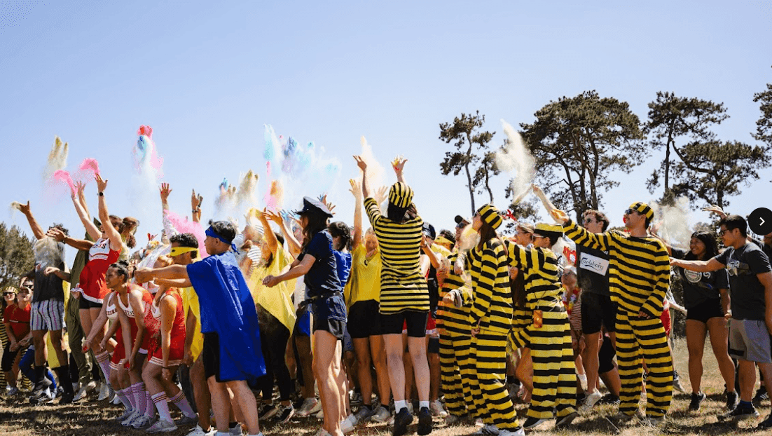 Large group of colleagues in costumes enjoying an outdoor team building activity, throwing colorful powder.