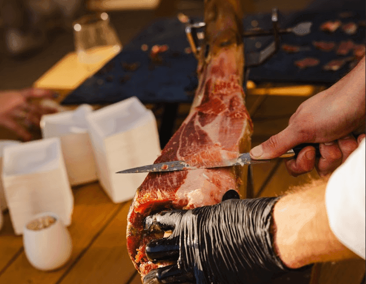 A caterer expertly slices a leg of cured ham for a corporate cocktail reception or networking event.
