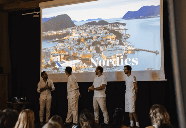 Four men present at a corporate seminar in an event space, with a large screen displaying a Nordic city.
