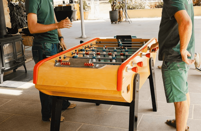 Two colleagues enjoy a game of foosball on an outdoor terrace during a corporate team building event.
