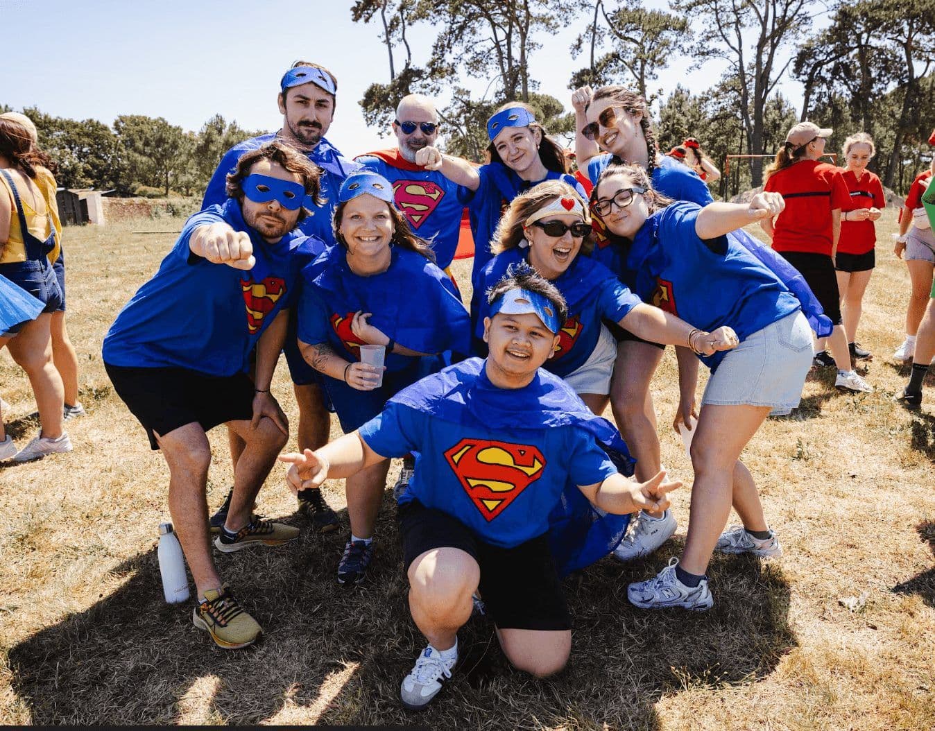 A large group of employees in Superman costumes posing happily during an outdoor team building activity.