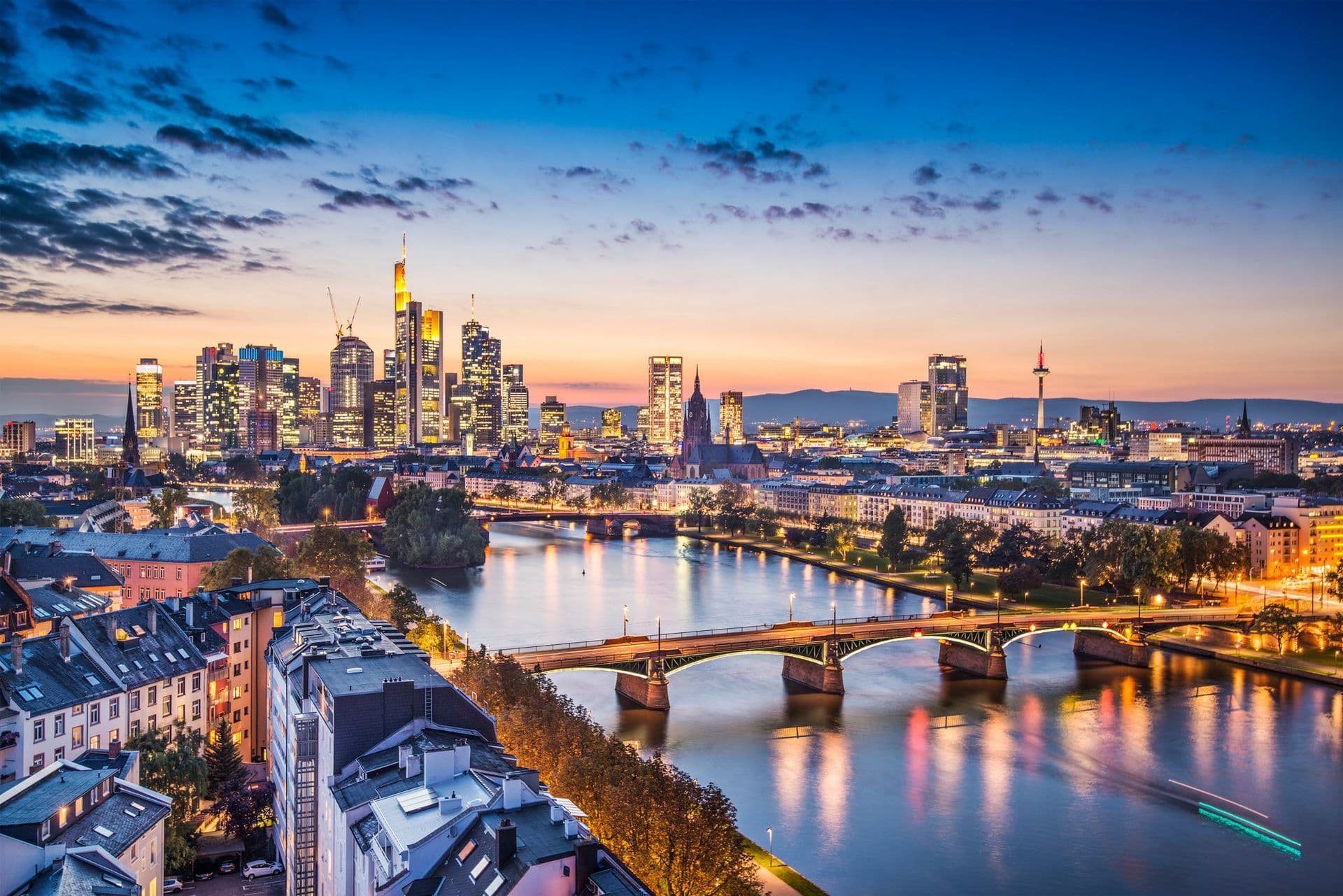 Frankfurt, Germany's vibrant skyline at dusk, with illuminated corporate buildings and bridges over the Main