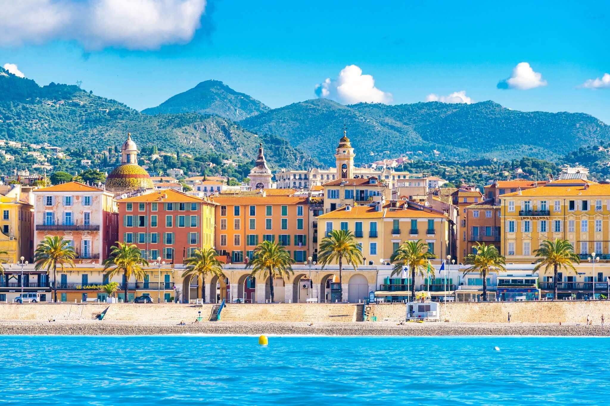 Vibrant coastal city of Nice, France, with colorful buildings, palm trees, beach, and blue sea