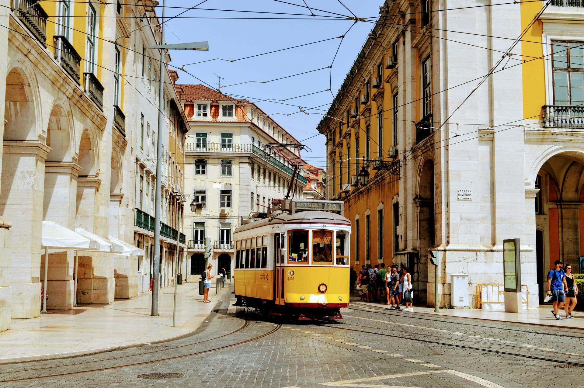 A classic yellow tram travels down a cobblestone street in historic Lisbon, Portugal.