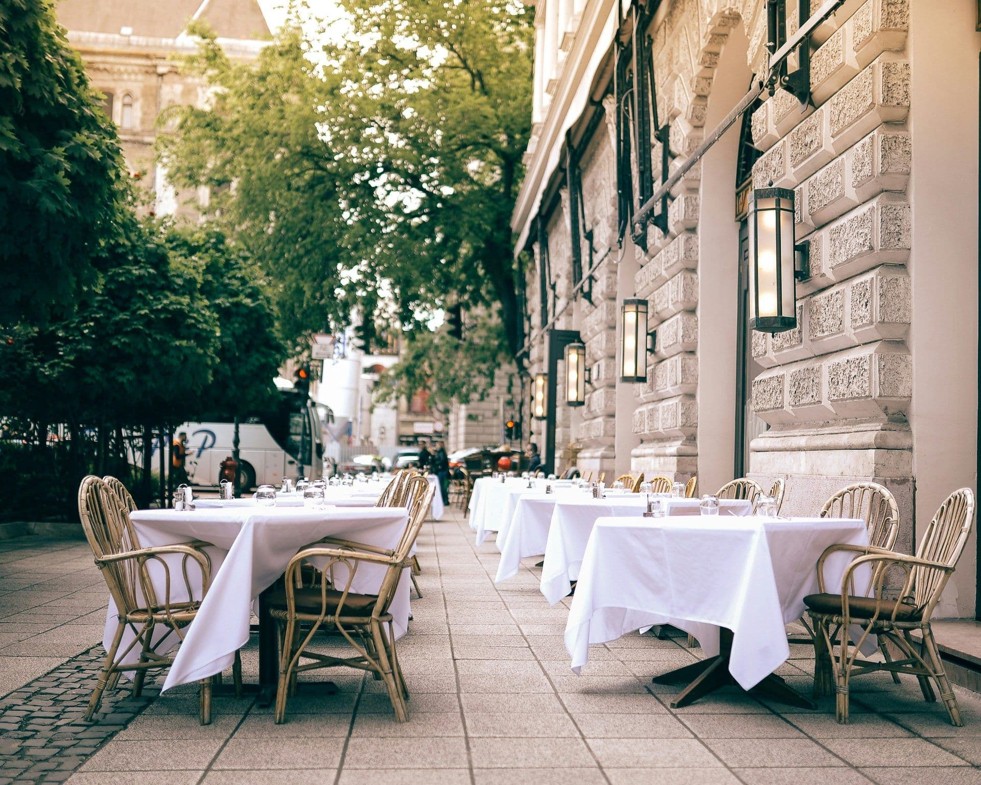 Outdoor restaurant terrace with white-clothed tables and wicker chairs, suitable for business lunches.