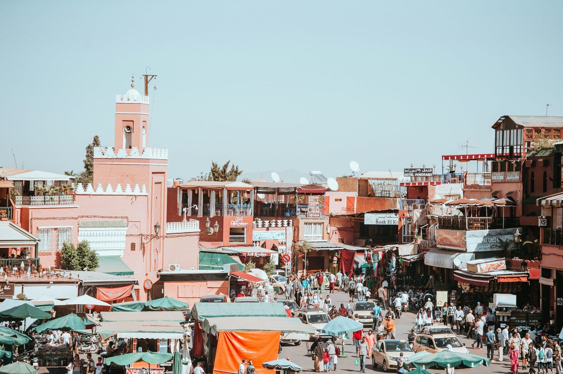 A bustling marketplace in Marrakech with a pink minaret, crowded streets, and rooftop terraces.