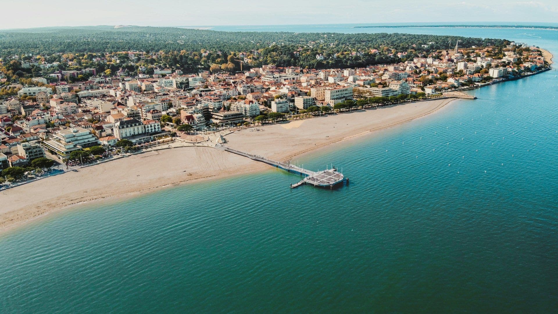 Aerial view of Arcachon, France, a waterfront venue with a sandy beach, pier, and turquoise bay.
